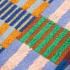 Close-up of a colourful striped textile with textured loops and woven sections in blue, green, orange, beige, and brown.