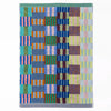 A rectangular bath mat with a colourful geometric patchwork pattern of vertical stripes and blocks in blue, green, pink, orange, purple, and yellow, finished with a stripey bottom borders.