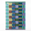 A rectangular woven textile bath mat with a multicolour geometric stripe pattern, featuring vertical bands of blue, green, pink, orange, and yellow on a white background.