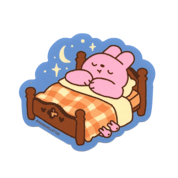 A sticker of a bunny cartoon sleeping on a bed tucked in with a check-pattern blanket. 