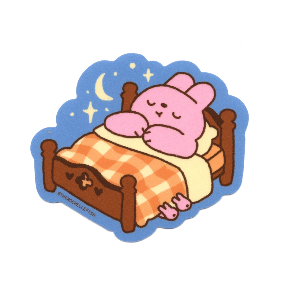 A sticker of a bunny cartoon sleeping on a bed tucked in with a check-pattern blanket. 