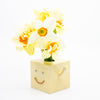 Square yellow vase with a face holding flowers on a white background