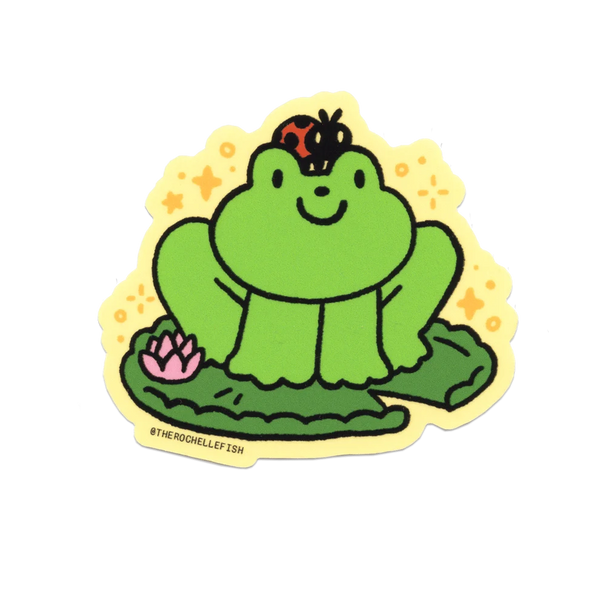 A die-cut sticker featuring a cute cartoon green frog sitting on a lily pad with a pink lotus flower and a ladybug on its head, set against a yellow starry background. The sticker has a yellow border and the handle @THEROCHHELFFISH printed on the bottom left.