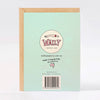 The back of a mint green textured greeting card with a kraft envelope behind it. The card features a circular logo for 'Wally Paper Co' logo illustration, website text, and a barcode.