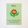 Iron-on embroidery patch with a colorful flower design on a green grid card.