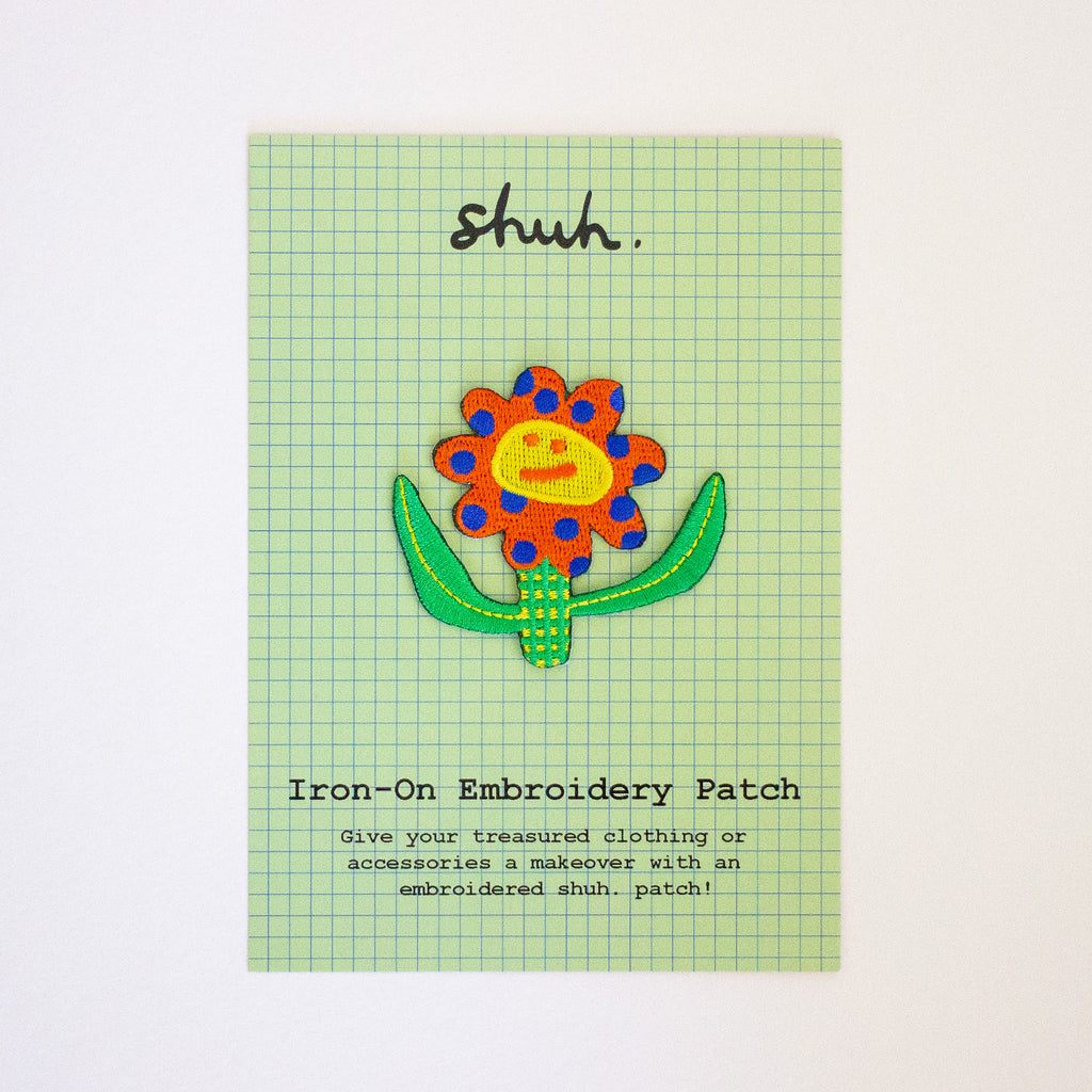 Iron-on embroidery patch with a colorful flower design on a green grid card.