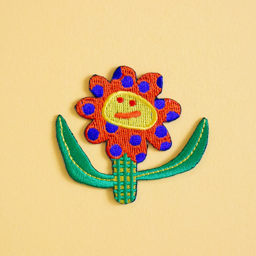 Colorful embroidered flower patch with a face on a yellow background