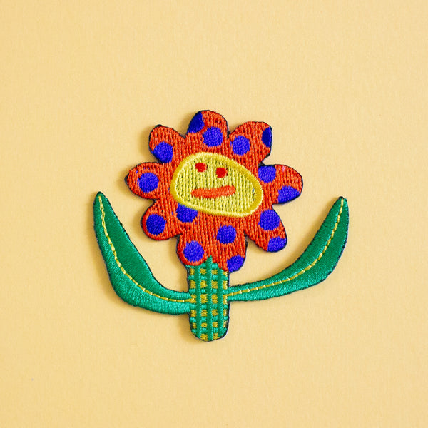 Colorful embroidered flower patch with a face on a yellow background