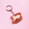 A keychain with an illustration of a lamb lying down with the words 'TOO CUTE TO DO MATHS' with a clear outline against a pink background. 