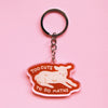 A keychain with an illustration of a lamb lying down with the words 'TOO CUTE TO DO MATHS' with a clear outline against a pink background. 
