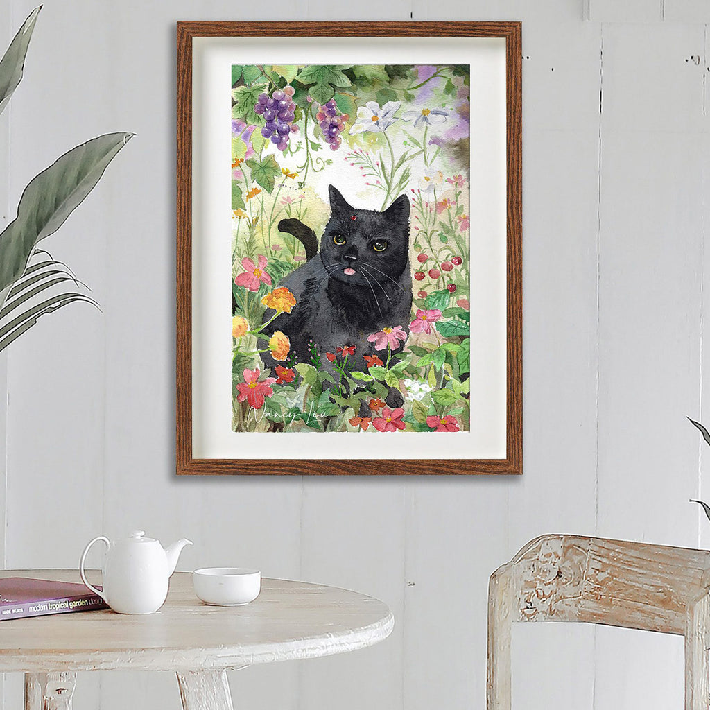 Framed artwork of a black cat among flowers on a wall above a table.