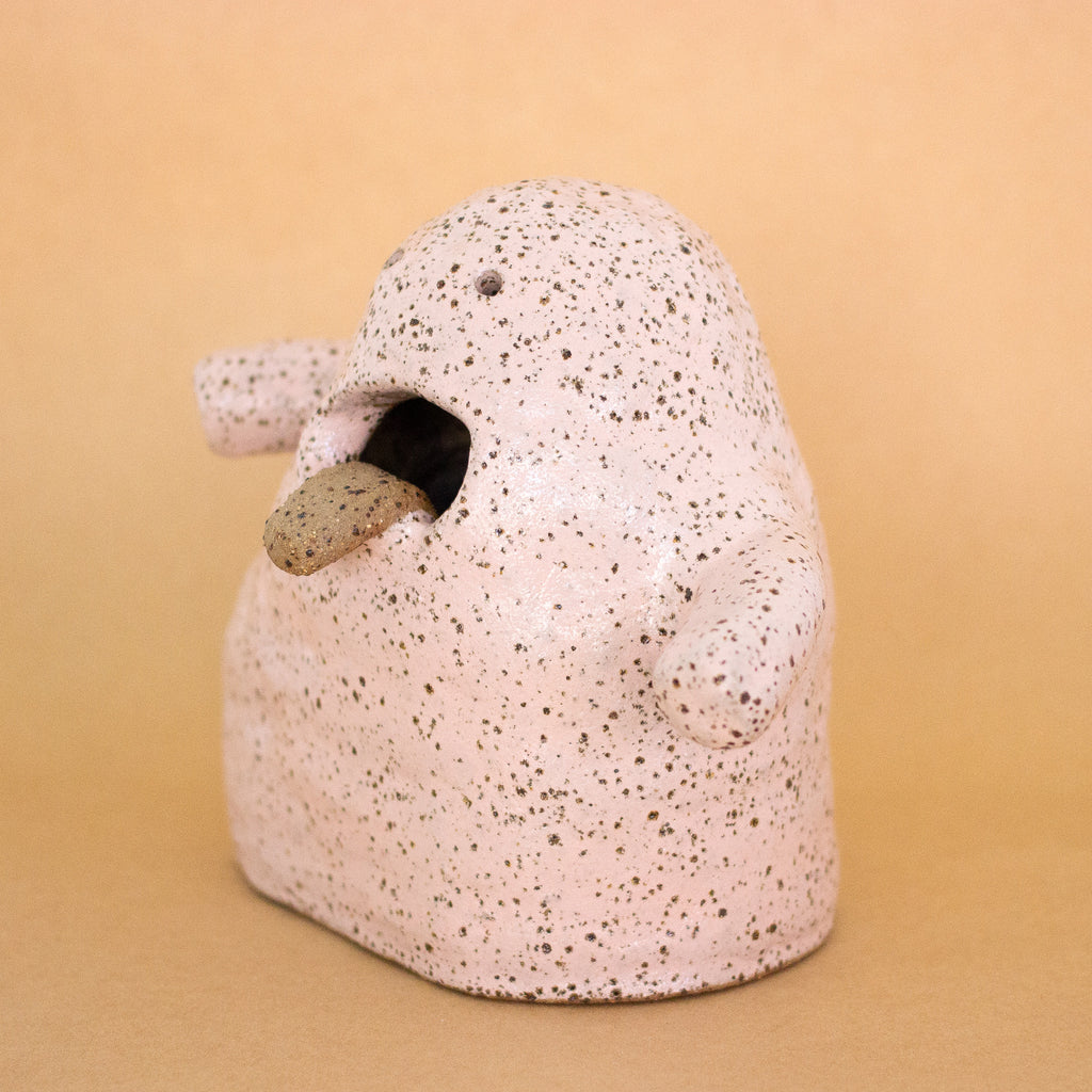 Side view of the Handbuilt ceramic figurine by shuh. with a speckled pink glaze, open mouth, and protruding tongue. Sculptural artwork made from stoneware clay for the Well Wishes exhibition.