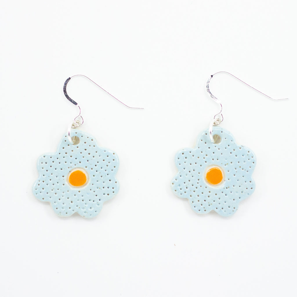 A photo of two bloom earrings with soft blue colouring, and orange centre. Polka dot effect and sterling silver hooks. 