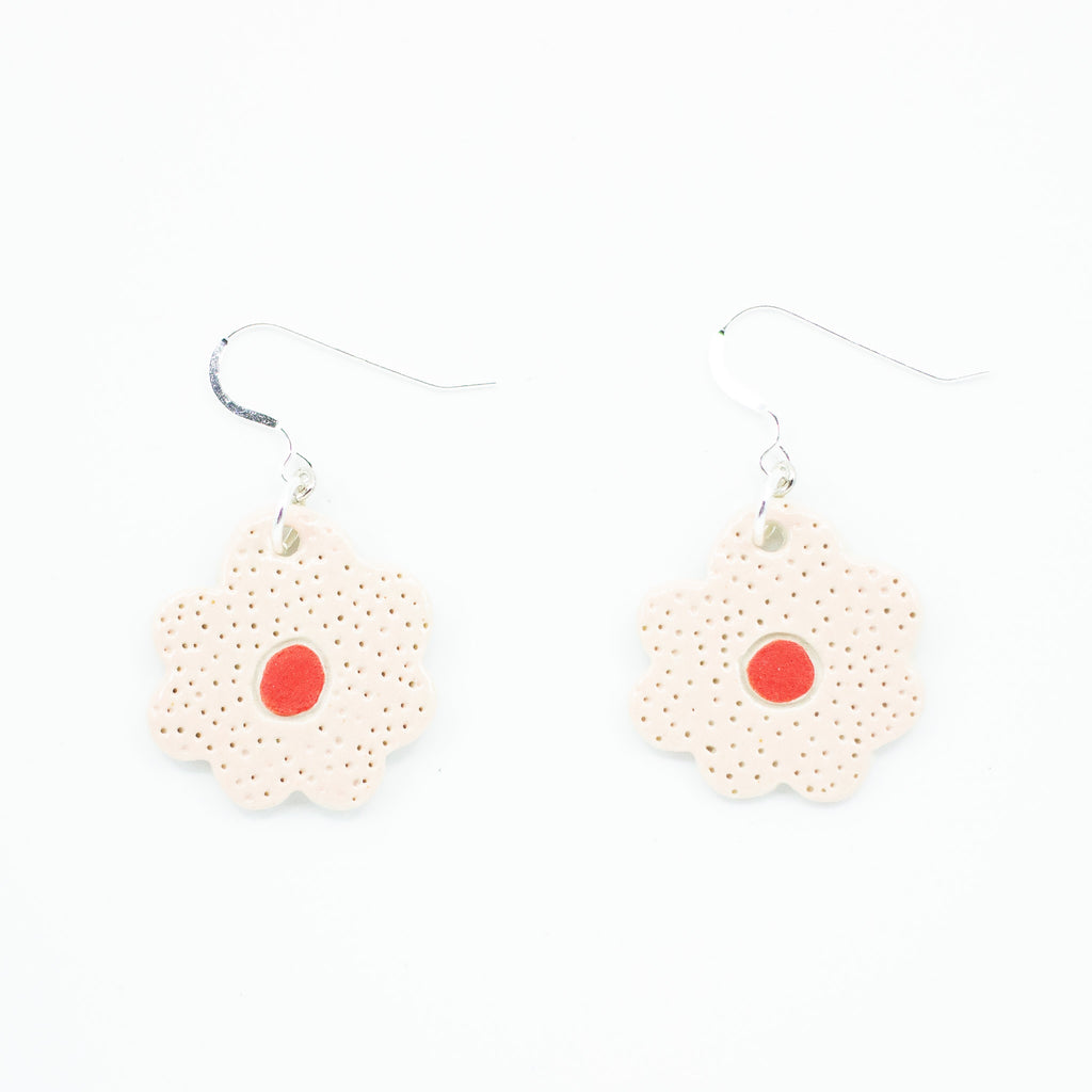A photo of two bloom earrings with soft pink colouring, and red centre. Polka dot effect and sterling silver hooks. 