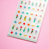 A sheet of small colourful flower stickers arranged on a translucent backing, photographed at an angle on a soft pink background.