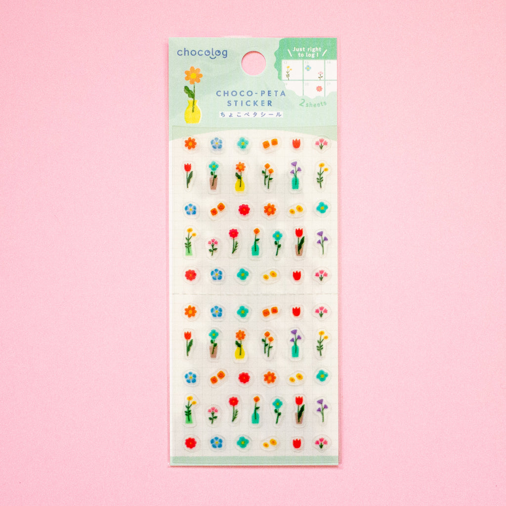 Sticker sheet featuring colourful mini flowers, leaves, and small decorative motifs on a white backing card with a mint green header, set against a solid pink background.