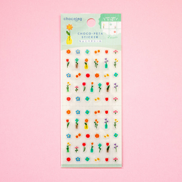 Sticker sheet featuring colourful mini flowers, leaves, and small decorative motifs on a white backing card with a mint green header, set against a solid pink background.