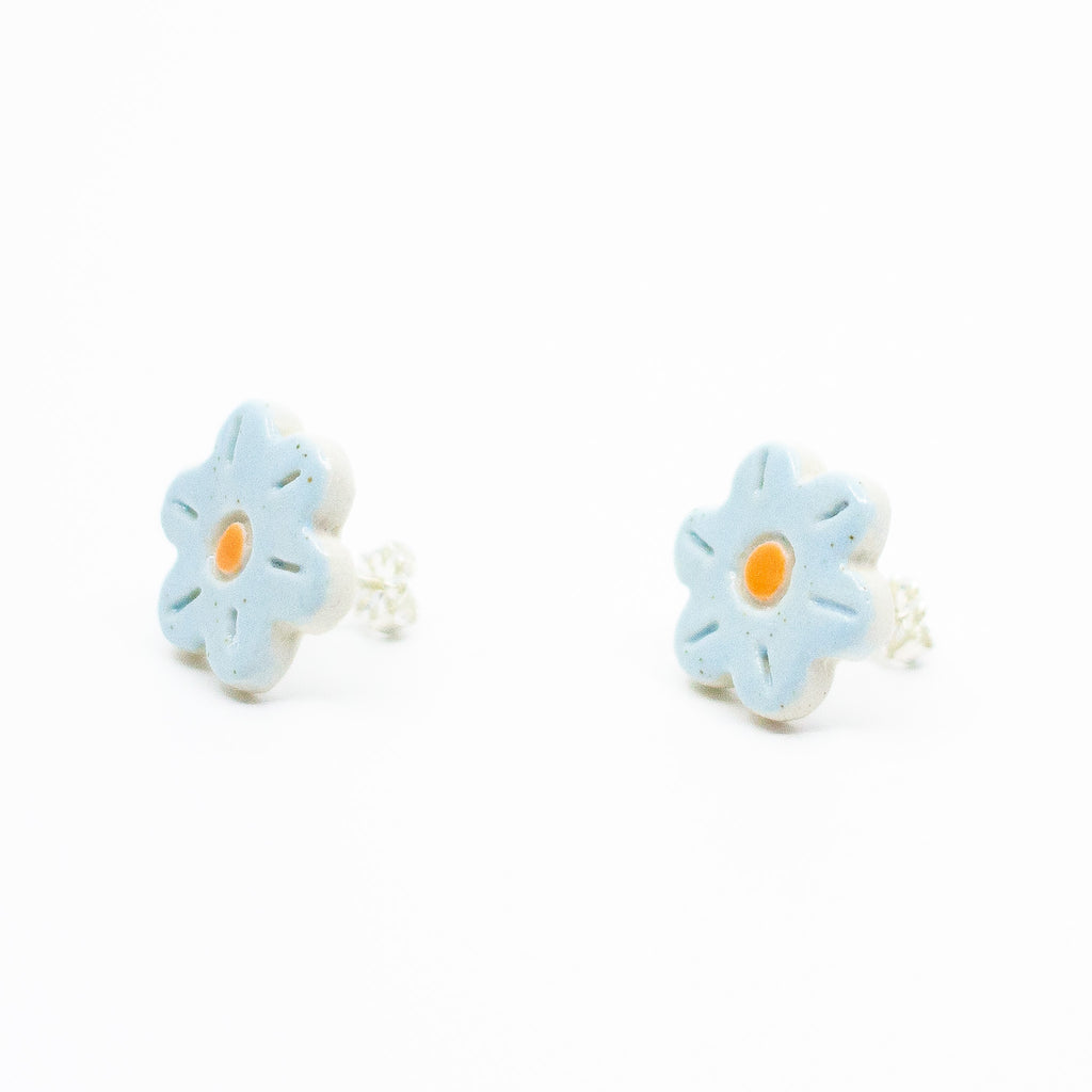A photo of the bluebell stud earrings. Ceramic earrings with a flower shape and light blue colour leaves with a orange centre. Side view shows sterling silver stud backings. 