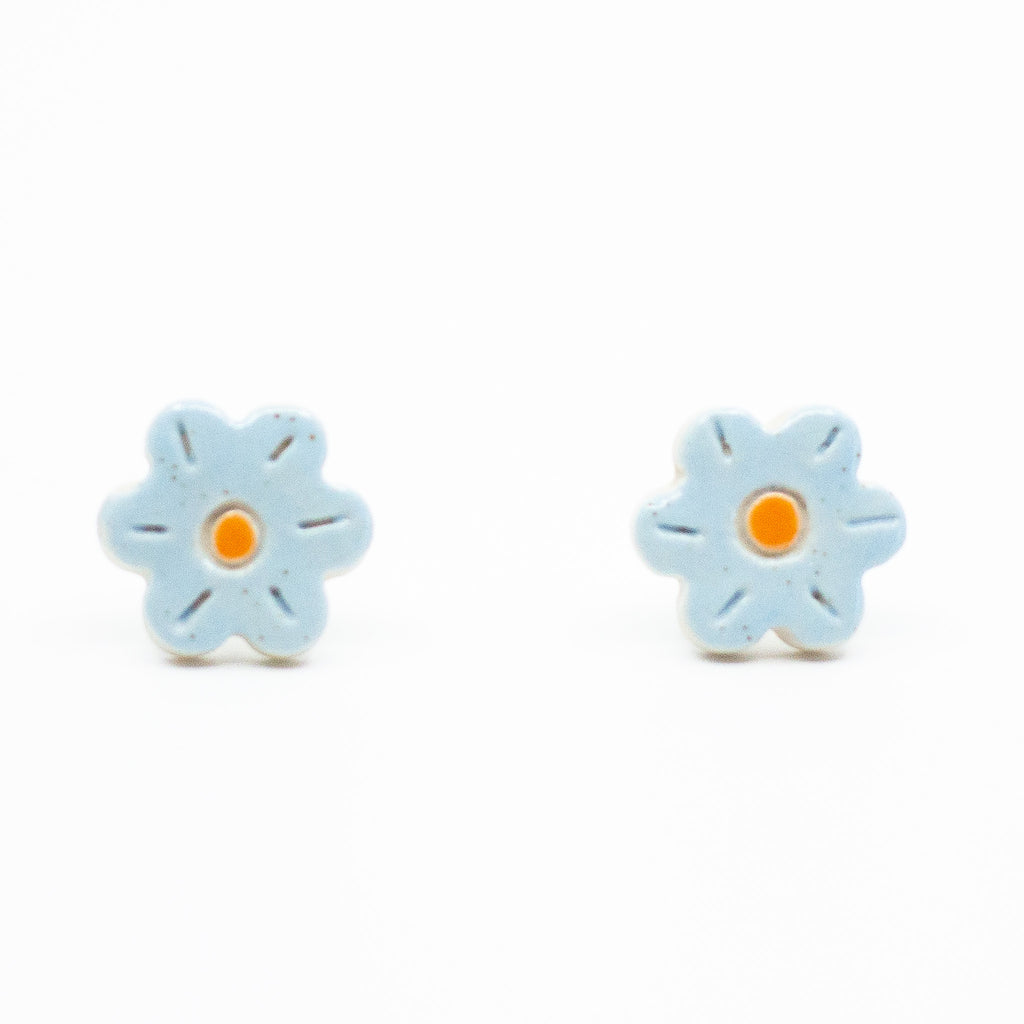 A photo of the bluebell stud earrings. Ceramic earrings with a flower shape and light blue colour leaves with a orange centre.