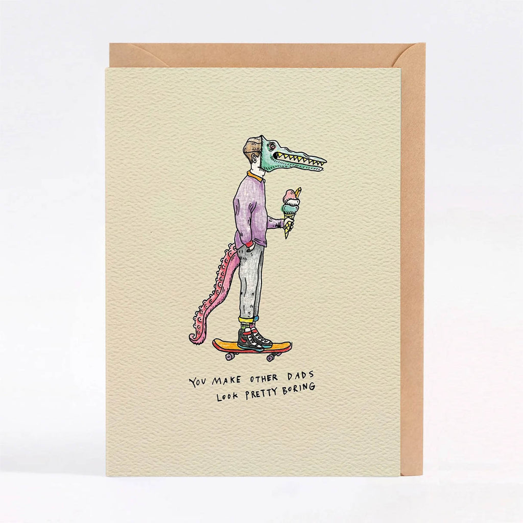 A card with a kraft envelope, featuring a whimsical illustration of a crocodile-headed person wearing a purple sweater and light pants while skateboarding and holding an ice cream cone. The card has a textured cream background with handwritten text at the bottom.