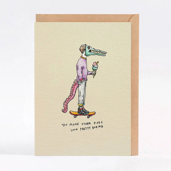 A card with a kraft envelope, featuring a whimsical illustration of a crocodile-headed person wearing a purple sweater and light pants while skateboarding and holding an ice cream cone. The card has a textured cream background with handwritten text at the bottom.