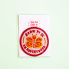 A circular embroidered patch featuring a smiling orange and yellow butterfly with the text 'BORN TO BE AN ADVENTURER' in red, displayed on a white backing card that reads 'YAN YAN CANDY NG'. The card is photographed against a pale mint green background.