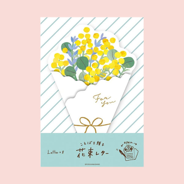 A envelope-style die-cut letter featuring a bouquet of yellow flowers wrapped in a white paper sleeve with gold foil script reading 'For you' and a gold bow. The card has diagonal mint green stripes, a light blue bottom band with Japanese text, and is photographed against a solid pale pink background.
