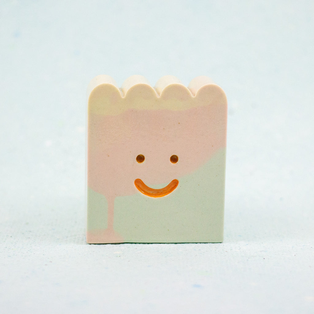 Small rectangular ceramic figure with scallop top and a smiley face design on a light gray background