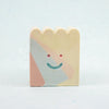 Small rectangular ceramic figure with scallop top and a smiley face design on a light gray background