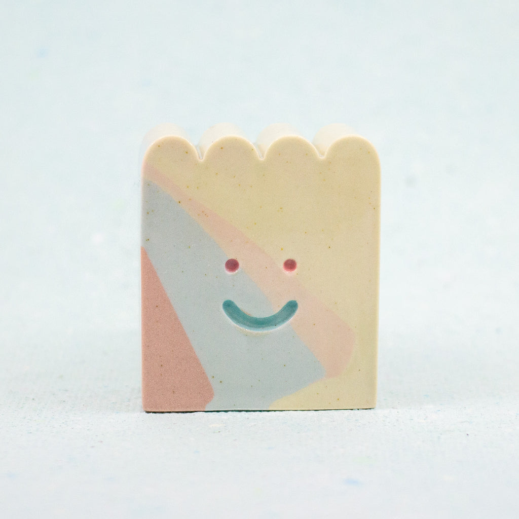 Small rectangular ceramic figure with scallop top and a smiley face design on a light gray background