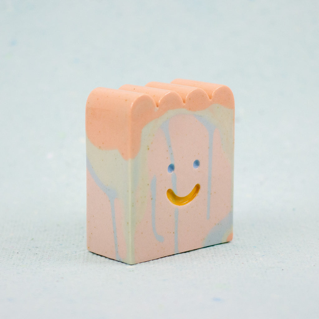Small rectangular ceramic figure with scallop top and a smiley face design on a light gray background