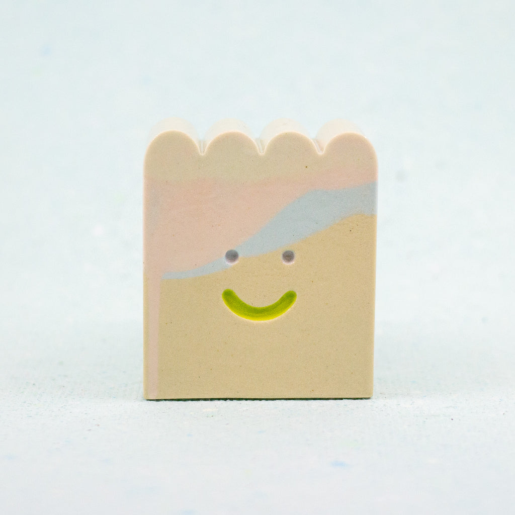 Small rectangular ceramic figure with scallop top and a smiley face design on a light gray background
