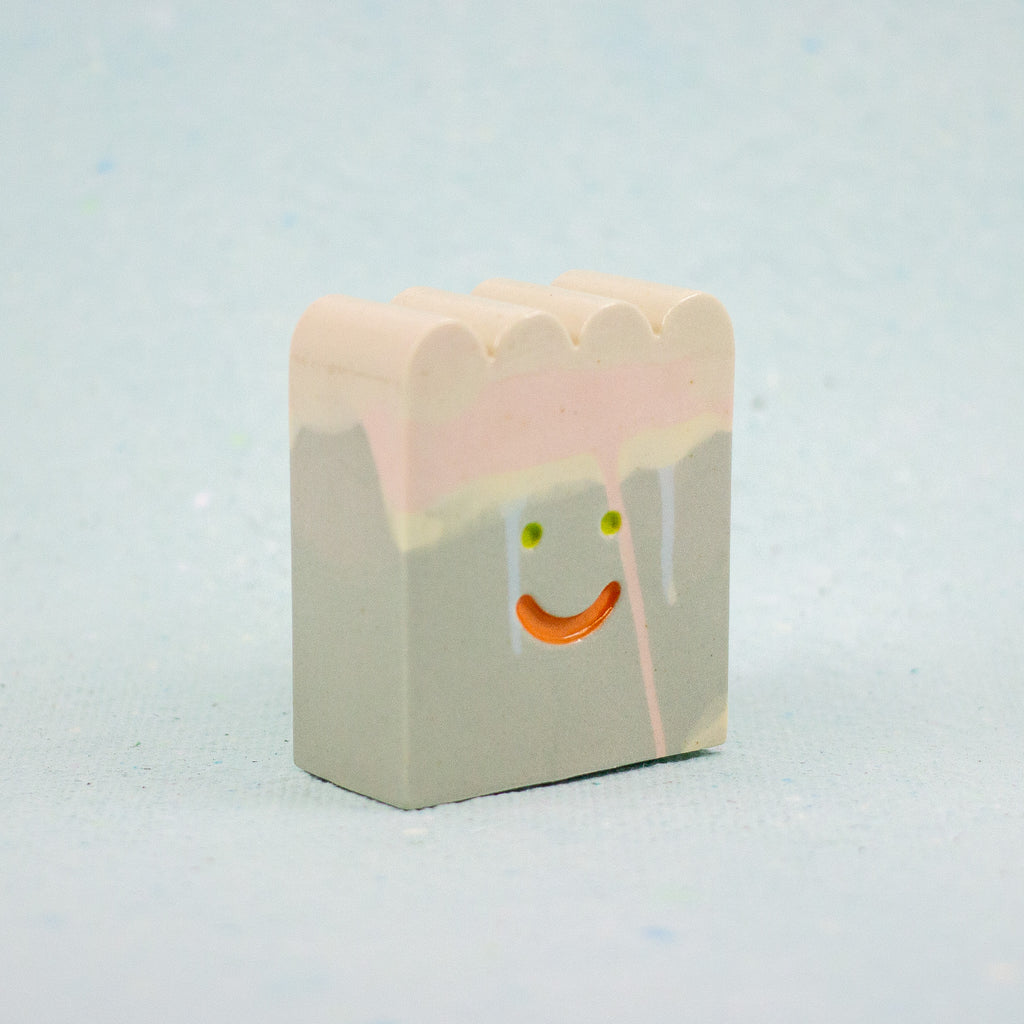 Small rectangular ceramic figure with scallop top and a smiley face design on a light gray background