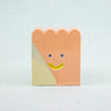 Small rectangular ceramic figure with scallop top and a smiley face design on a light gray background