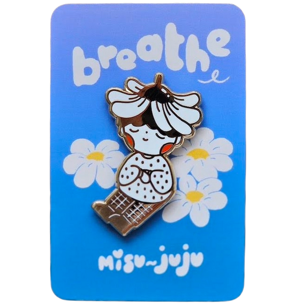 A cute enamel pin of a girl with a flower crown sitting among daisies, mounted on a blue backing card that reads 'breathe' and 'Misu Juju'.