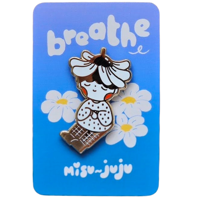 A cute enamel pin of a girl with a flower crown sitting among daisies, mounted on a blue backing card that reads 'breathe' and 'Misu Juju'.
