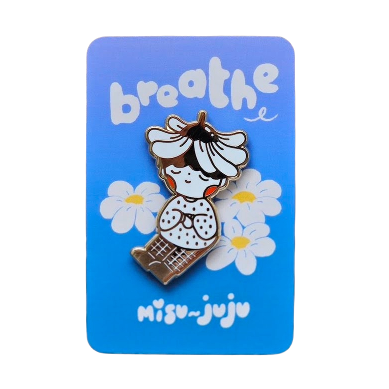 A cute enamel pin of a girl with a flower crown sitting among daisies, mounted on a blue backing card that reads 'breathe' and 'Misu Juju'.