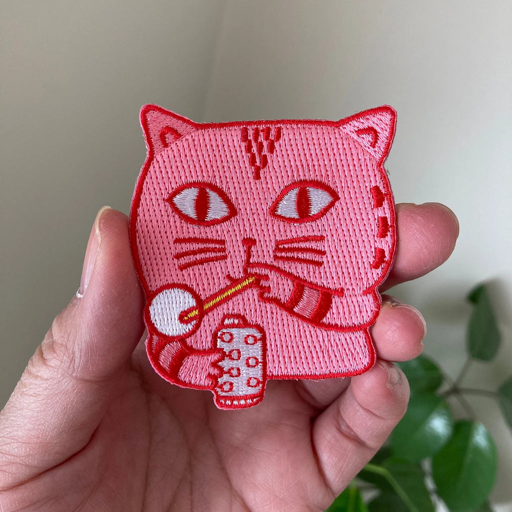 Pink embroidered cat patch held in a hand with a blurred background