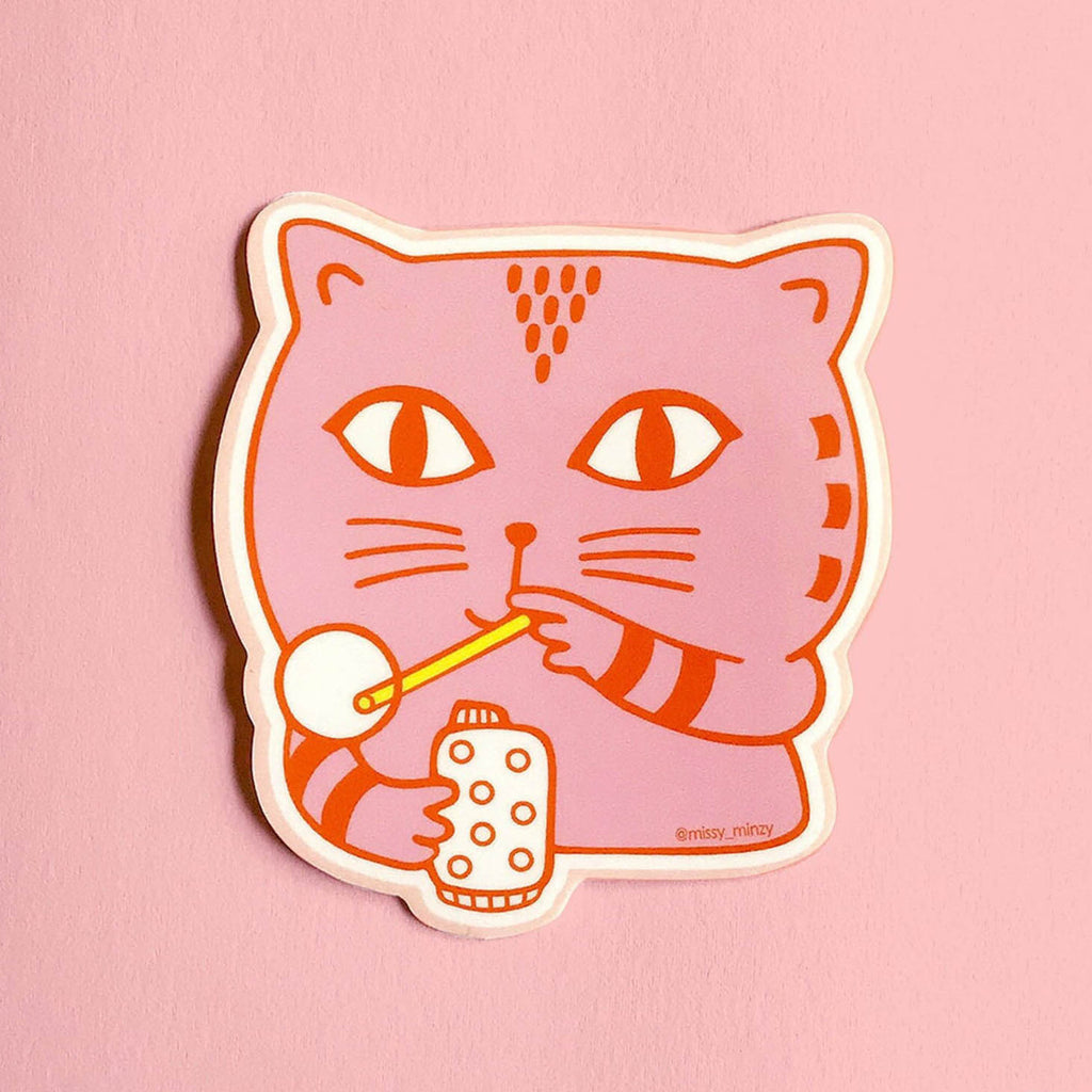 A die-cut sticker featuring a pink cartoon cat with red outlines, holding a yellow bubble wand and bubble popper, shown on a solid pink background.