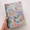 Hand holding a journal featuring a range of stickers including glitter stickers of sea-themed cartoons. 