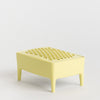 A pale yellow plastic soap dish with a textured, perforated top and four short legs, shown on a seamless light grey background.