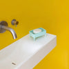 A four-legged mint soap dish with a soap in it sitting on a sink. 
