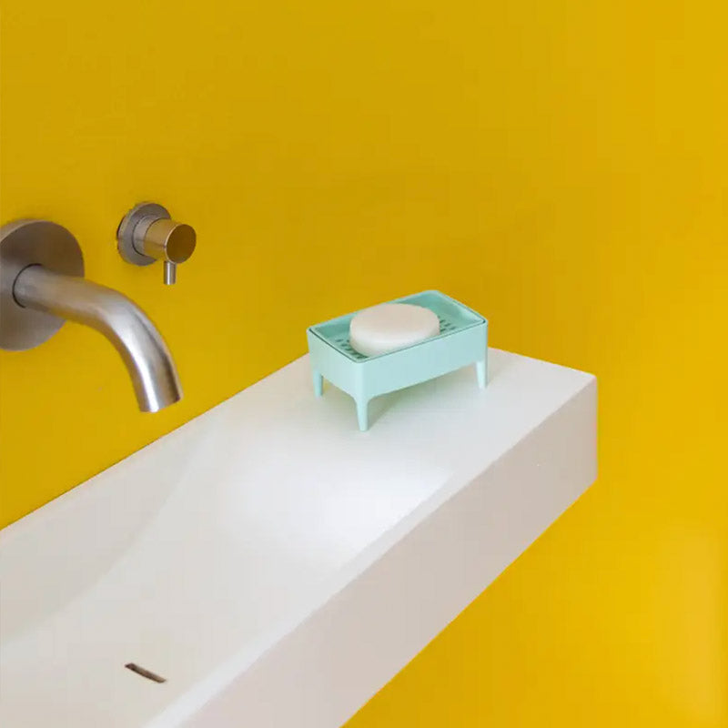 A four-legged mint soap dish with a soap in it sitting on a sink. 