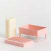 Pink-coloured soap dish on a clean white background: a cream-coloured rectangular soap bar, a dusty pink footed tray, and a matching pink textured lid.