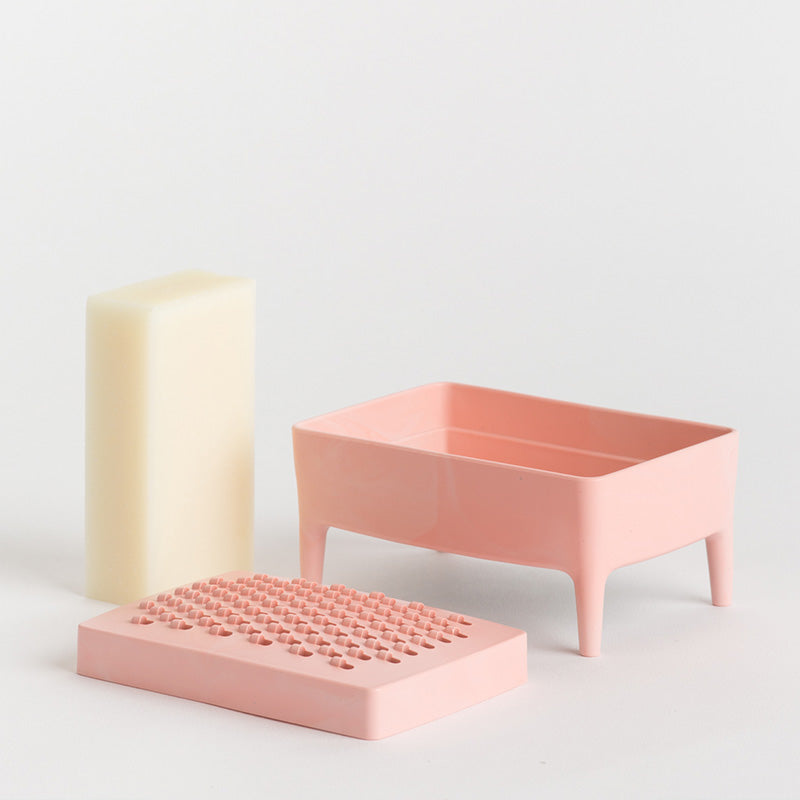 Pink-coloured soap dish on a clean white background: a cream-coloured rectangular soap bar, a dusty pink footed tray, and a matching pink textured lid.