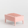 A small pink soap dish with a textured, raised pattern on the top surface and four short legs, photographed on a clean white studio background.