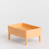 A small rectangular peach-coloured plastic tray with four legs and a perforated top, photographed on a clean light grey background.