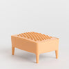 A peach-coloured soap dish with a textured surface on top and four short legs, photographed on a seamless light grey background.