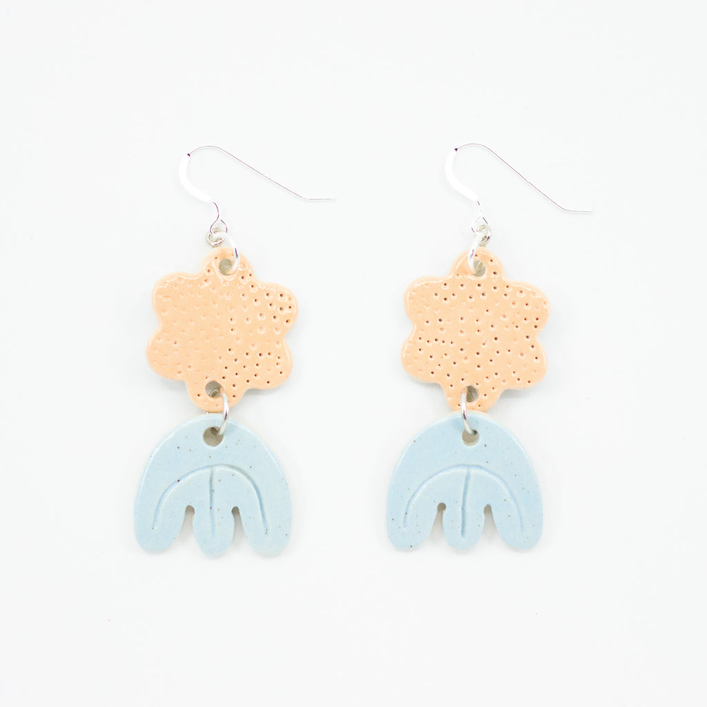 Picture features a closeup of two ceramic earrings with sterling silver hooks. Each earring has two ceramic beads, the first bead is peach coloured and polka dots in a daisy shape. The Second bead is tulip shaped in a pastel blue glaze. 