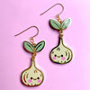 Pair of garlic-shaped earrings with smiling faces on a pink background